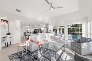 A modern living room with a glass coffee table, white sofas, and a pool area visible through large windows.