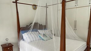 Een hemelbed met baldakijn, een nachtkastje met een klok en een klein bijzetmeubel.