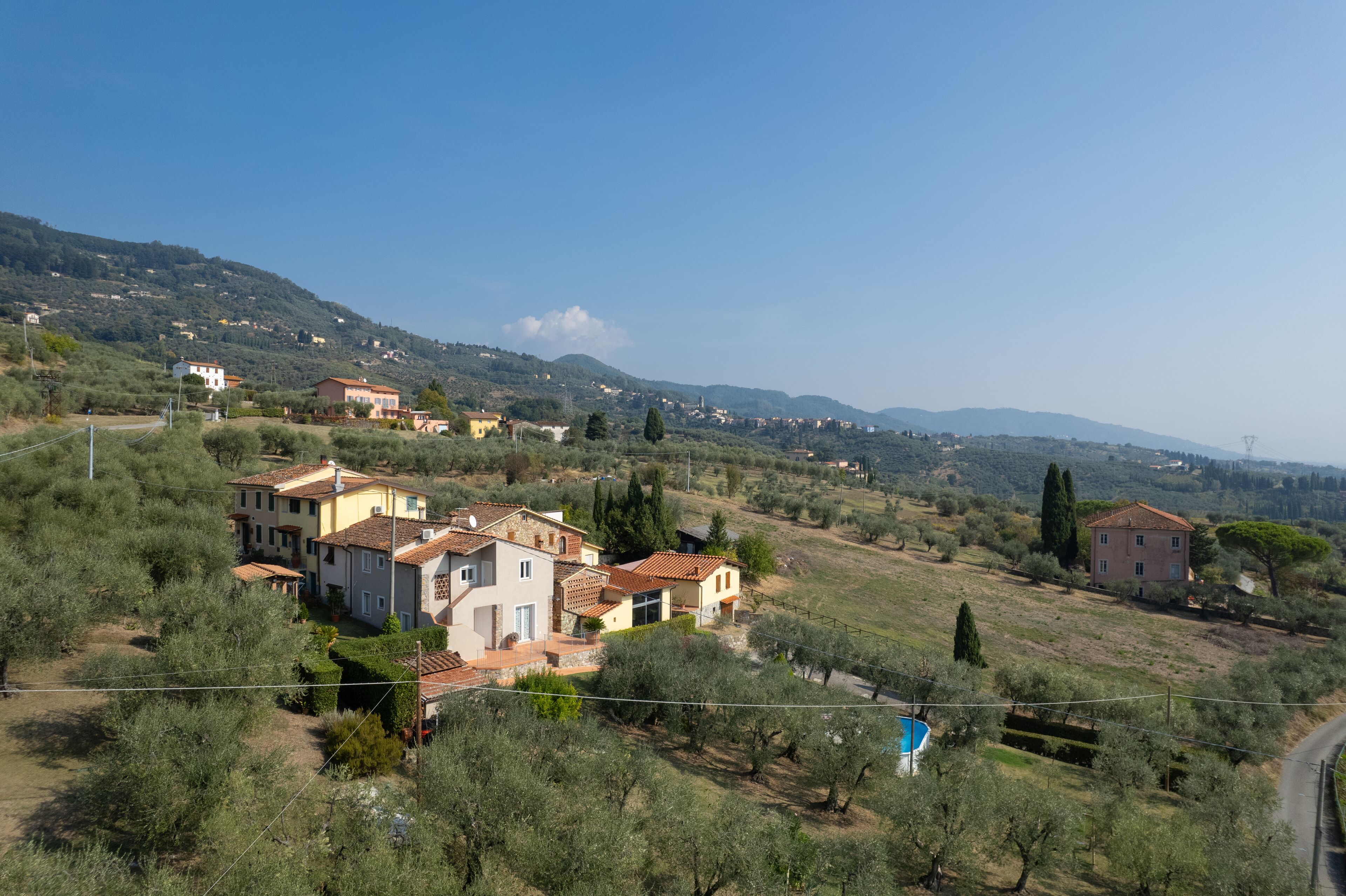 A hillside village with traditional Mediterranean architecture, including terracotta-roofed houses and a prominent villa with a swimming pool.