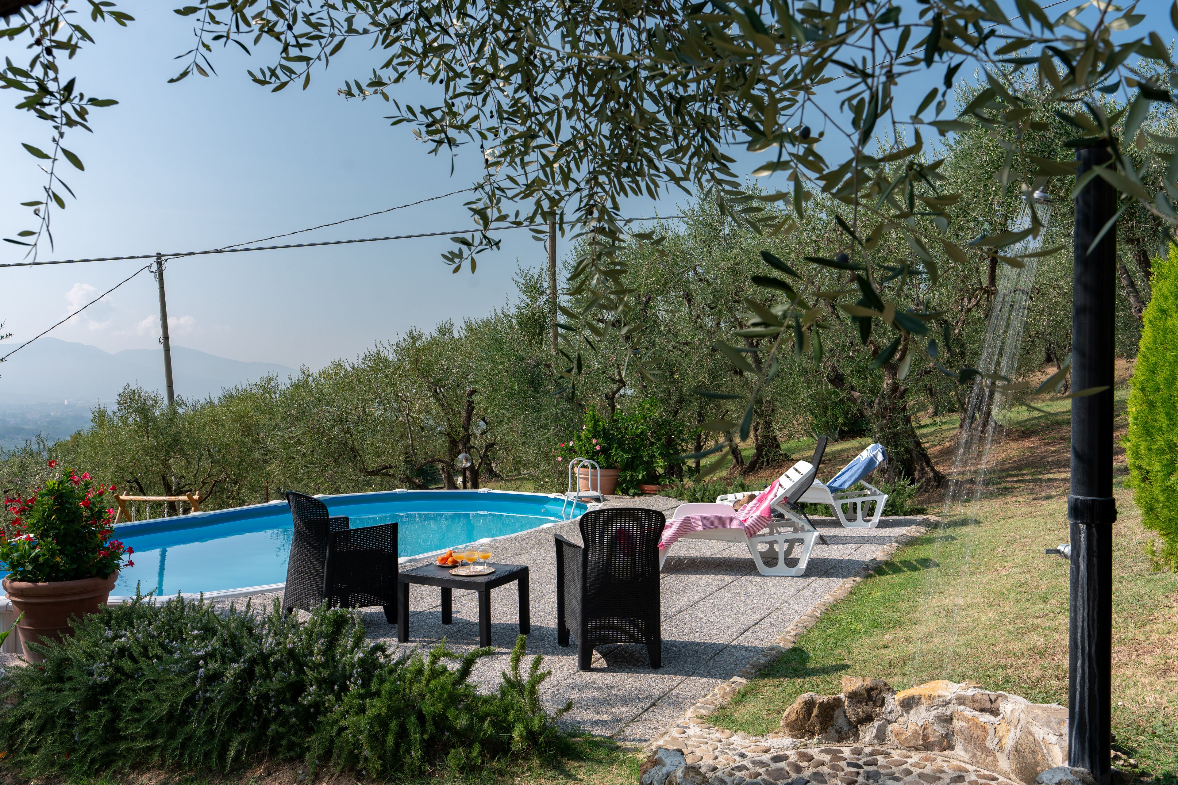 Ein Swimmingpool mit Liegestühlen und einem Tisch, umgeben von viel Grün und einem Kiesweg.