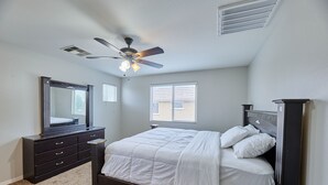 Ein Schlafzimmer mit Bett, Kommode, Deckenventilator und Fenstern.