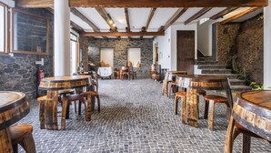 A rustic interior with stone walls, wooden beams, and round tables with stools. - Casas da Luz - Casa da Latada by Homie (Ponta do Sol)