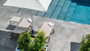 An outdoor swimming pool with two lounge chairs and a table, surrounded by grey tiles and green plants. - Casas da Luz - Casa da Latada by Homie (Ponta do Sol)
