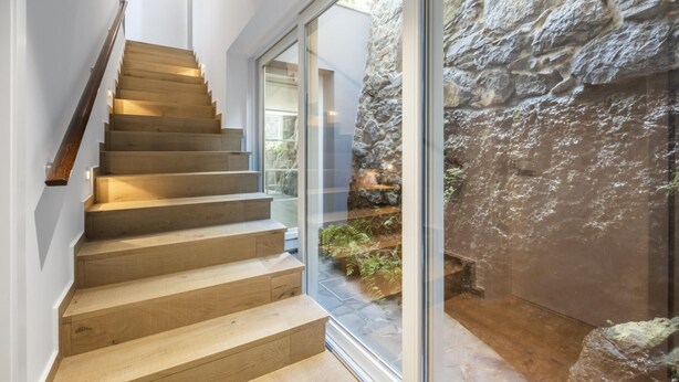 A modern staircase with wooden steps and a glass door leading to a stone wall and outdoor garden. - Casas da Luz - Casa da Latada by Homie (Ponta do Sol)