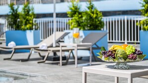 A poolside area with lounge chairs, a table with a fruit bowl, and a blue wall with greenery. - Casas da Luz - Casa da Latada by Homie (Ponta do Sol)