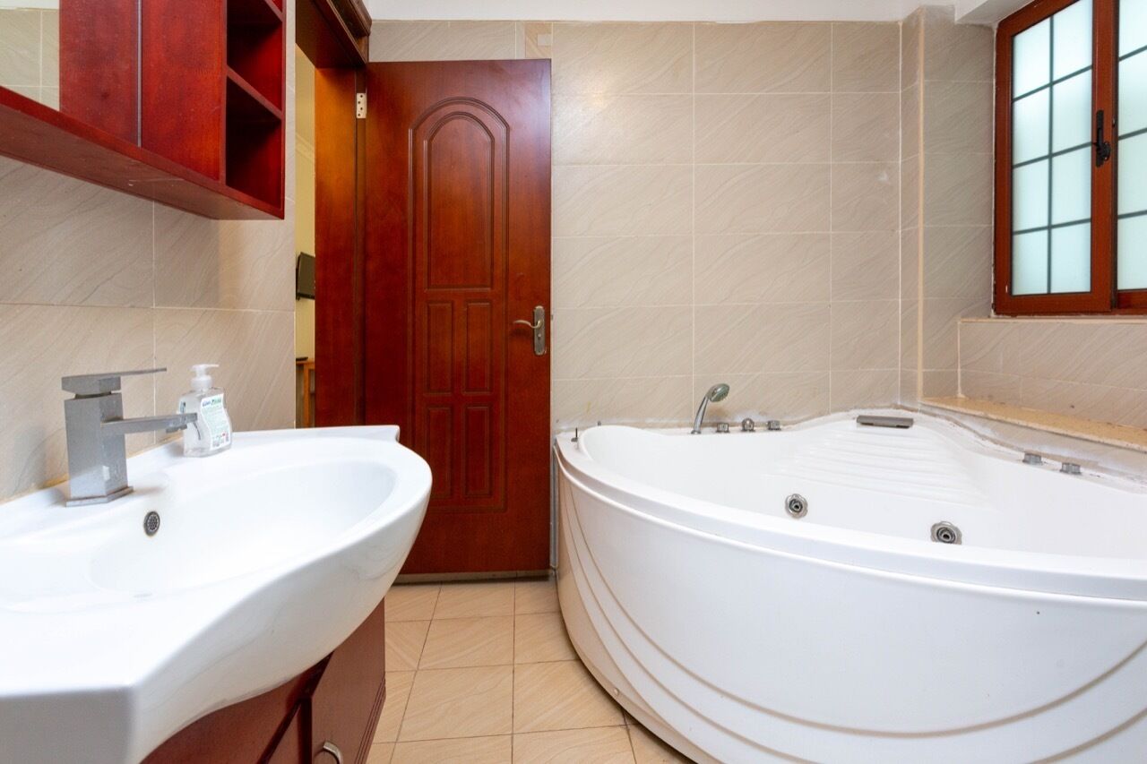 A bathroom with a wooden door, a white bathtub, and a sink with a mirror.