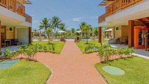 Un patio de hotel con un camino central de ladrillo, mobiliario exterior y palmeras.