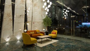 Eine Lobby mit Marmorwand, einer Topfpflanze, gelben Sesseln, einem Couchtisch und hängenden, kugelförmigen Lampen.
