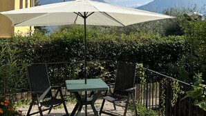 An outdoor patio with a table and chairs, a large umbrella, and a view of mountains in the background. - Lakeview Lakecomo 4seasons, Terrace, 30m to Lake! (Acquaseria)