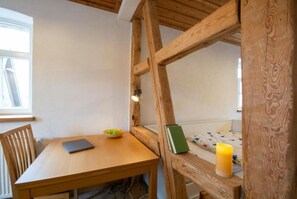 Una mesa de madera con un cuenco de fruta y un libro, una silla y una estructura de vigas de madera.