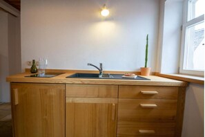 Una cocina con encimera de madera, dos lavabos, una planta en maceta y una ventana.