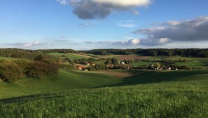 Un paisaje rural con colinas onduladas, casas dispersas y cielo despejado.