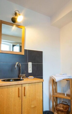 Un baño con tocador de madera, un lavamanos moderno, un espejo y una lámpara fijada a la pared.