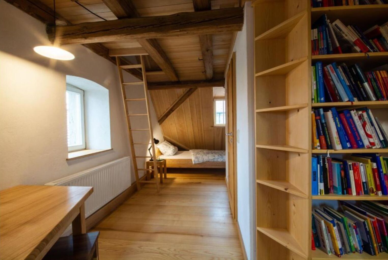 Ein Zimmer mit Hochbett, Holzschreibtisch, Bücherregal und einer Leiter.