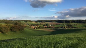Un paisaje rural con colinas onduladas, casas dispersas y cielo despejado.