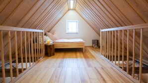 A high-ceilinged attic bedroom with a sloped wooden roof, a single bed, and two cribs. - Apartment Walnut (Oberscheinfeld)