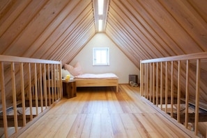 Ein Schlafzimmer im Dachgeschoss mit hohen Decken, einem geneigten Holzbalken und einem Bett sowie zwei Babybetten.