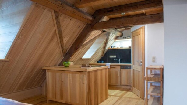 A compact kitchen with wooden cabinets and a small island, featuring a skylight and a view of the adjacent room. - Apartment Walnut (Oberscheinfeld)