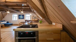A modern kitchen with wooden beams, a built-in stove, and a dining area with a blue sofa. - Apartment Walnut (Oberscheinfeld)