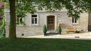 A stone building with a central entrance, two potted plants, a wooden bench, and a small table with flowers. - Apartment Walnut (Oberscheinfeld)