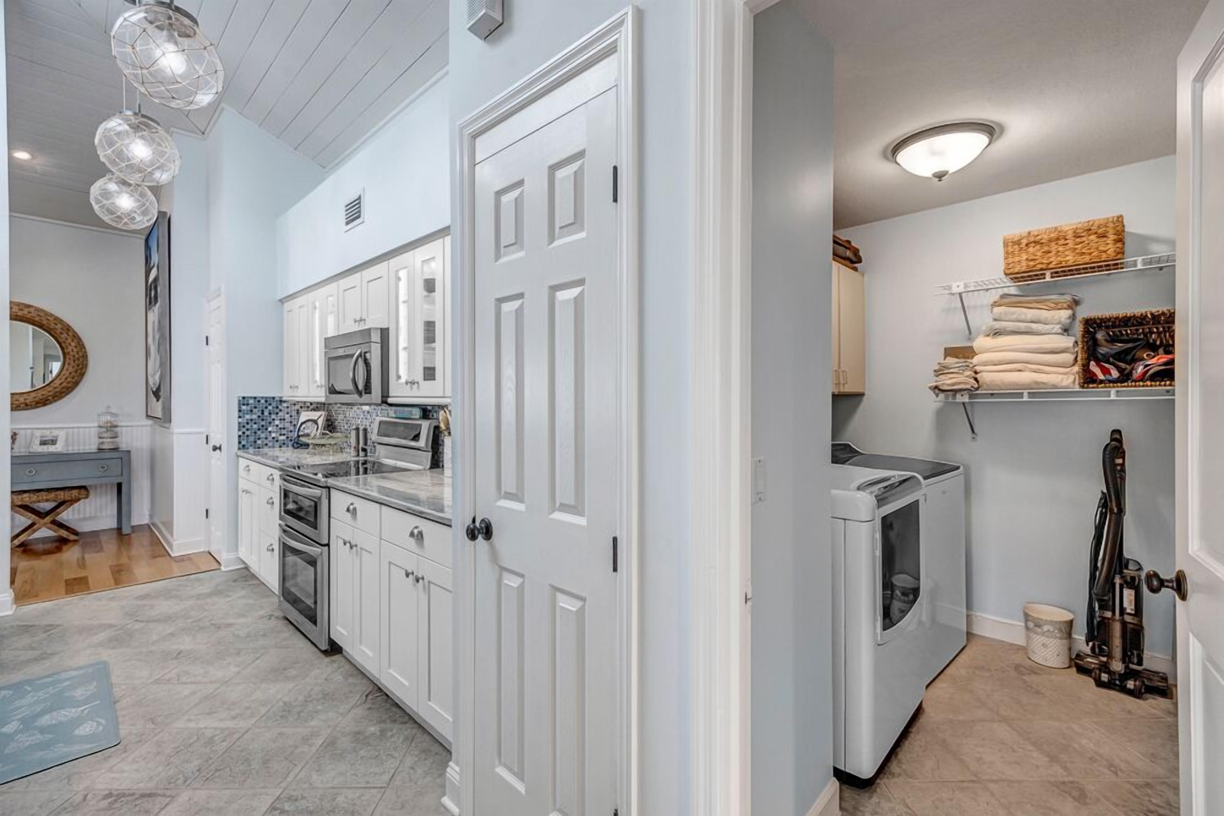 A modern kitchen with white cabinets, a built-in microwave, and a laundry area with a washing machine.
