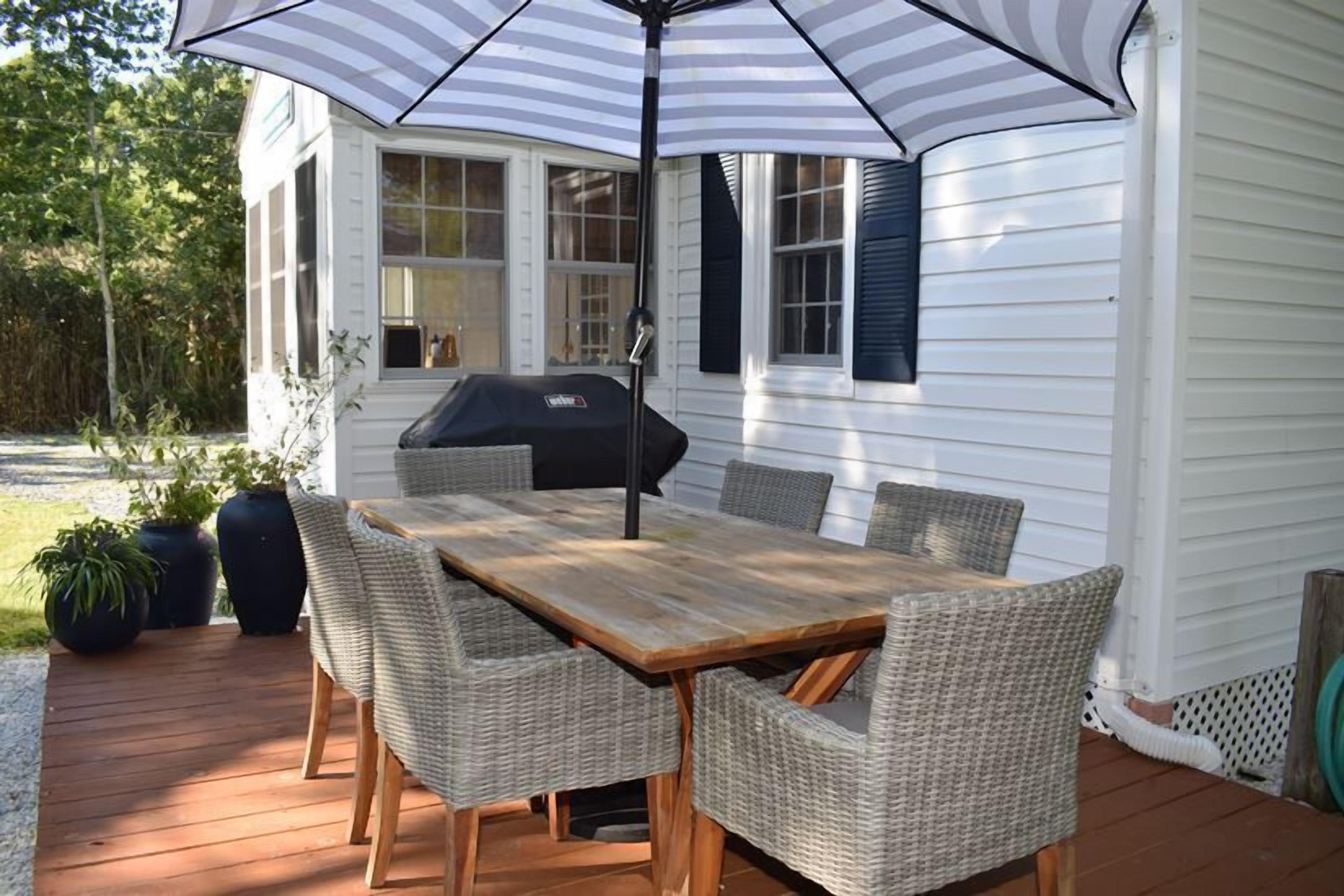 A wooden deck with a table and chairs, a grill, and an umbrella.