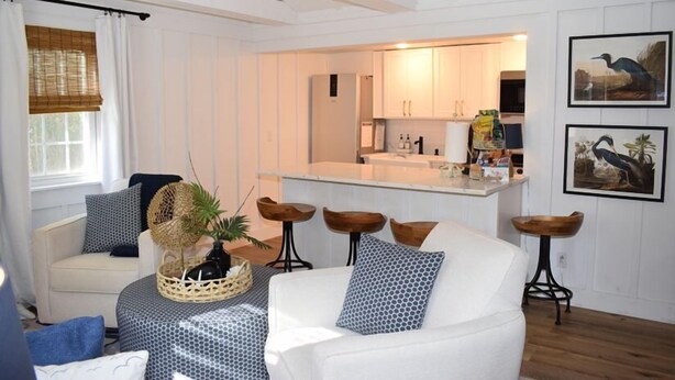A modern living room with a white sofa, a coffee table, and a kitchen area in the background.