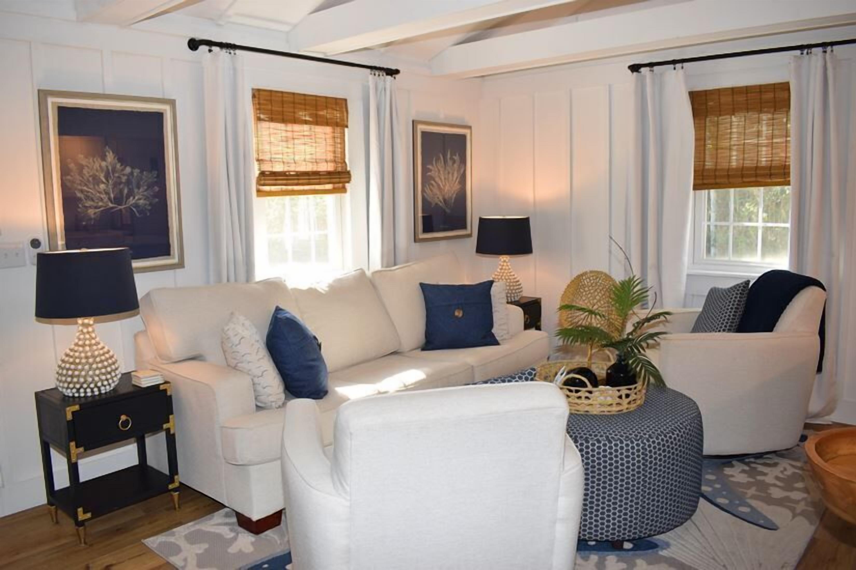 A living room with a white sofa, blue cushions, a side table with a lamp, and a patterned ottoman.