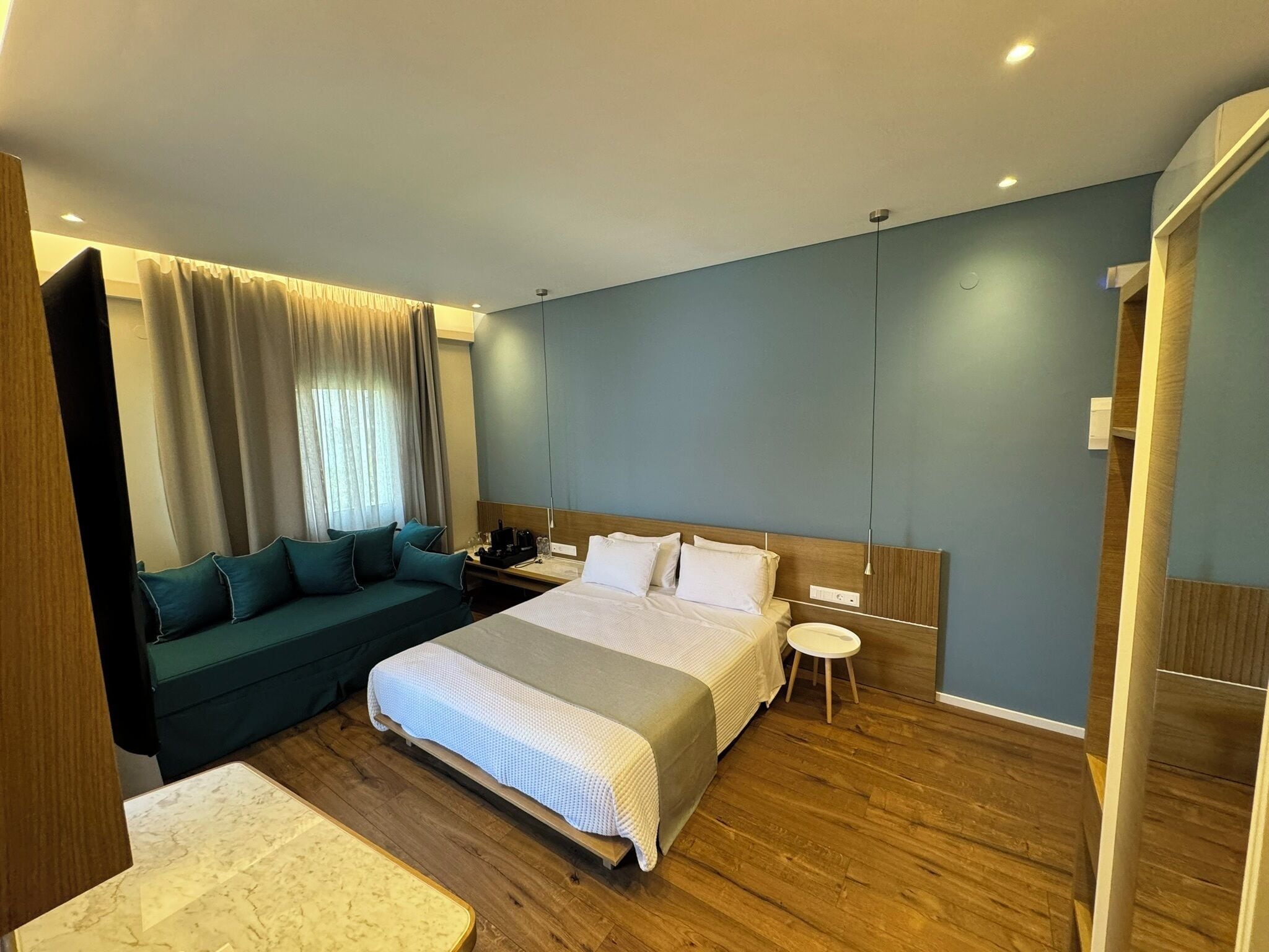 A modern hotel room with a bed, a sofa, a small table, and a nightstand.