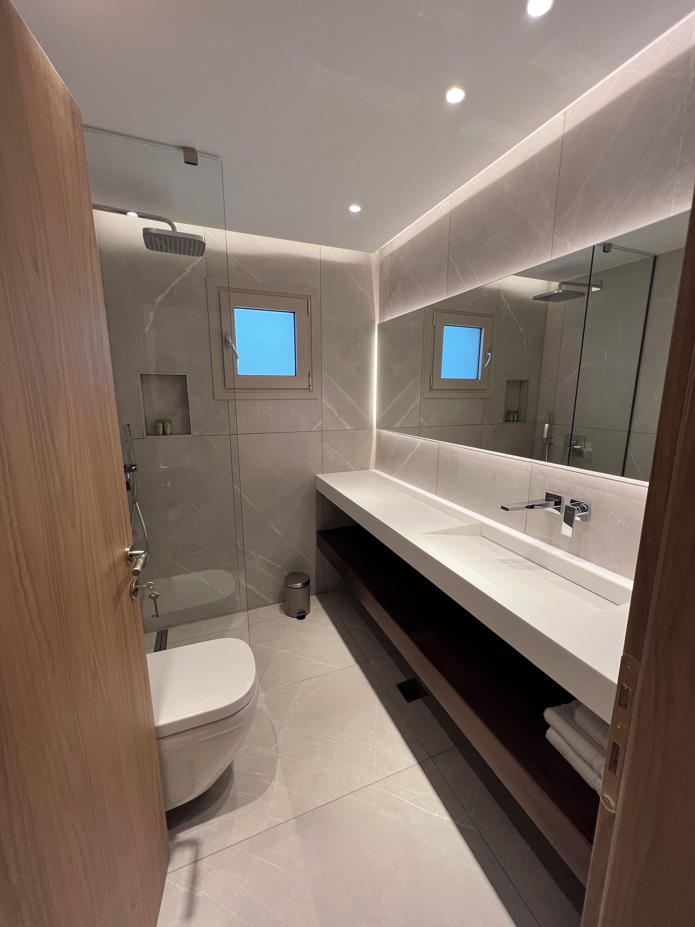 A modern bathroom with a glass shower enclosure, a white toilet, and a large mirror above the sink.