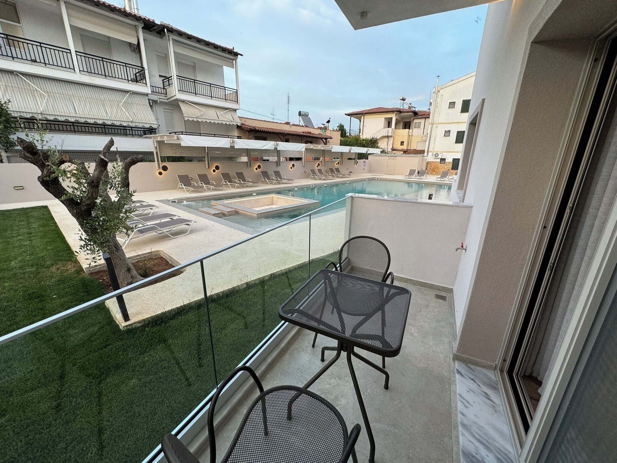 A balcony with a pool, lounge chairs, and a table.