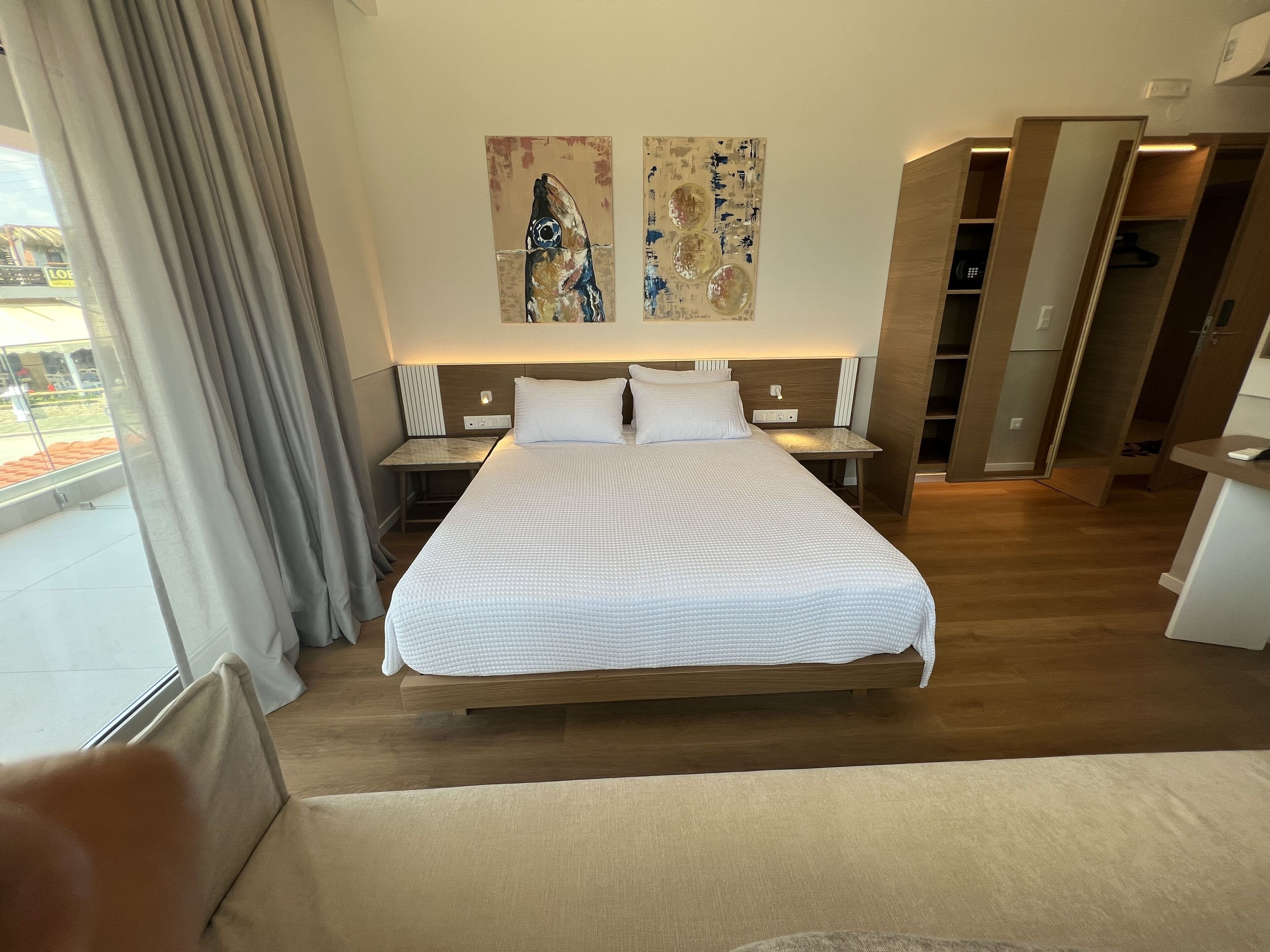 Una habitació d'hotel amb un llit gran, una taula de nit, cortines a la finestra i obra d'art a la paret.