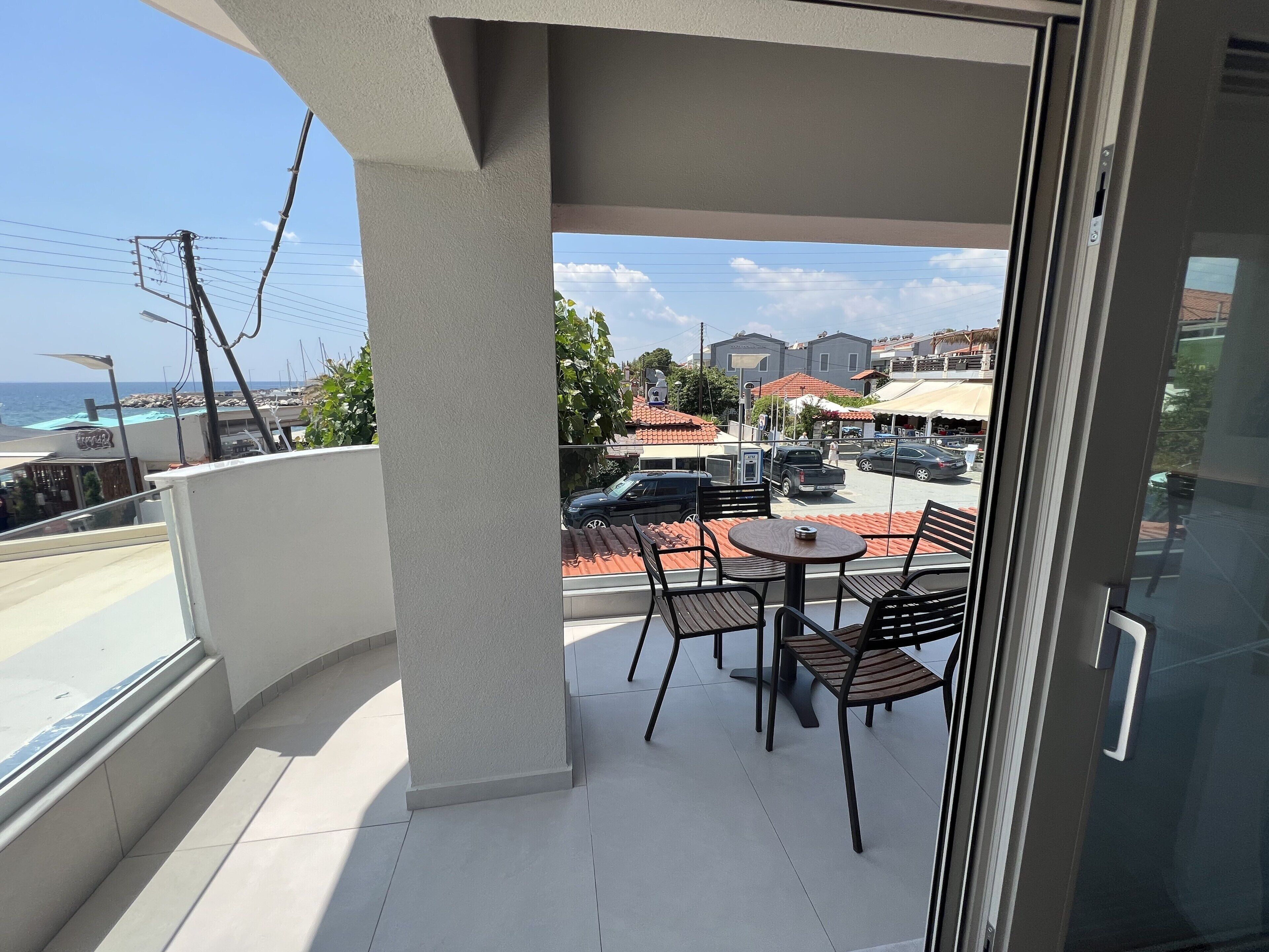 Un balcon avec vue sur la mer, une table avec des chaises et une porte vitrée.