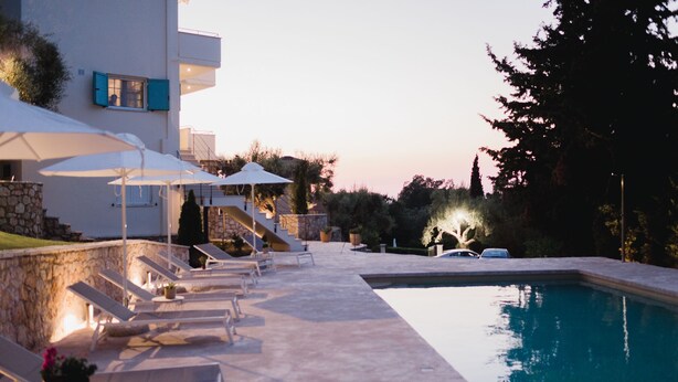 A pool area with lounge chairs and umbrellas, a stone wall, and a car parked nearby. - Locanda villas Lefkada B (Lefkada)