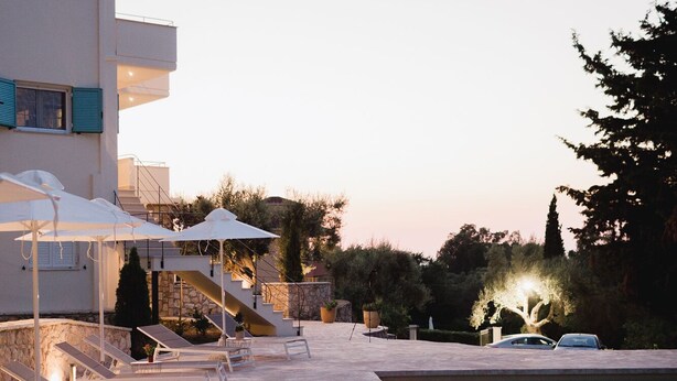 A poolside area with lounge chairs and umbrellas, a stone wall, and a building with a balcony. - Locanda Villa Lefkada C (Lefkada)