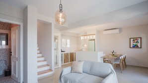 A modern living room with a sofa, a dining area with a table and chairs, a kitchen with a refrigerator, and a staircase. - Locanda Villa Lefkada C (Lefkada)