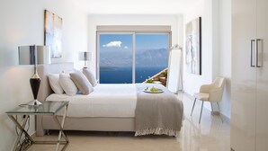 Una camera da letto moderna con un letto grande, un tavolino in vetro, una sedia e vista sul mare.