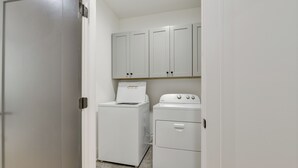 A laundry room with a washing machine and dryer, white cabinets above, and a door leading to another room.