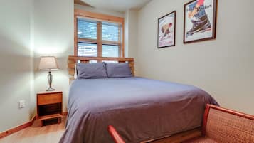 Une chambre à coucher comprenant un lit, une table de chevet, une lampe, une fenêtre avec des stores et deux tableaux encadrés accrochés au mur.