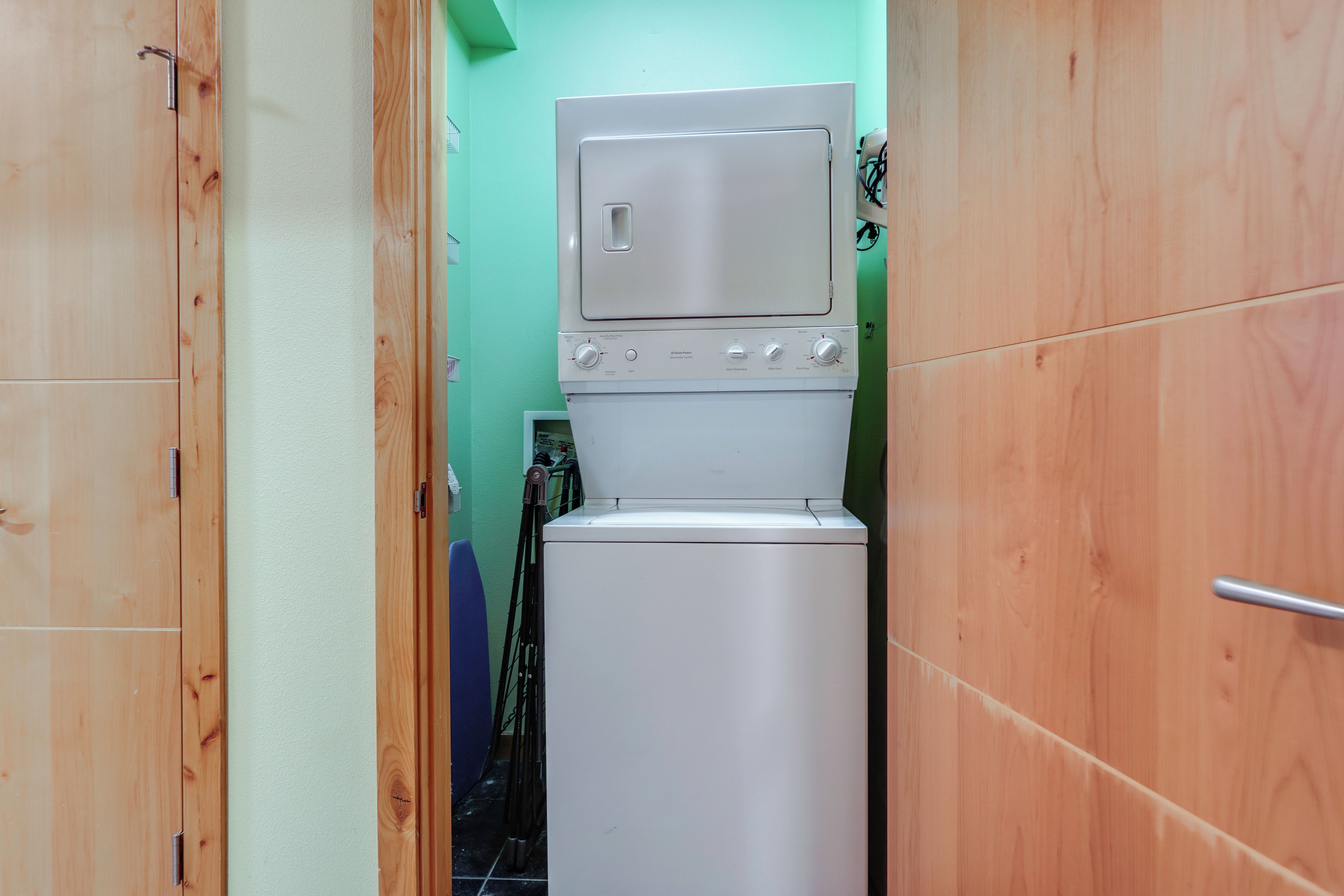 A compact laundry room with a stacked washer and dryer, wooden cabinets, and a green wall.