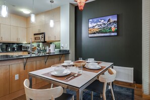 Une cuisine moderne avec des meubles en bois, des appareils en acier inoxydable et un coin repas avec une table dressée pour deux personnes.