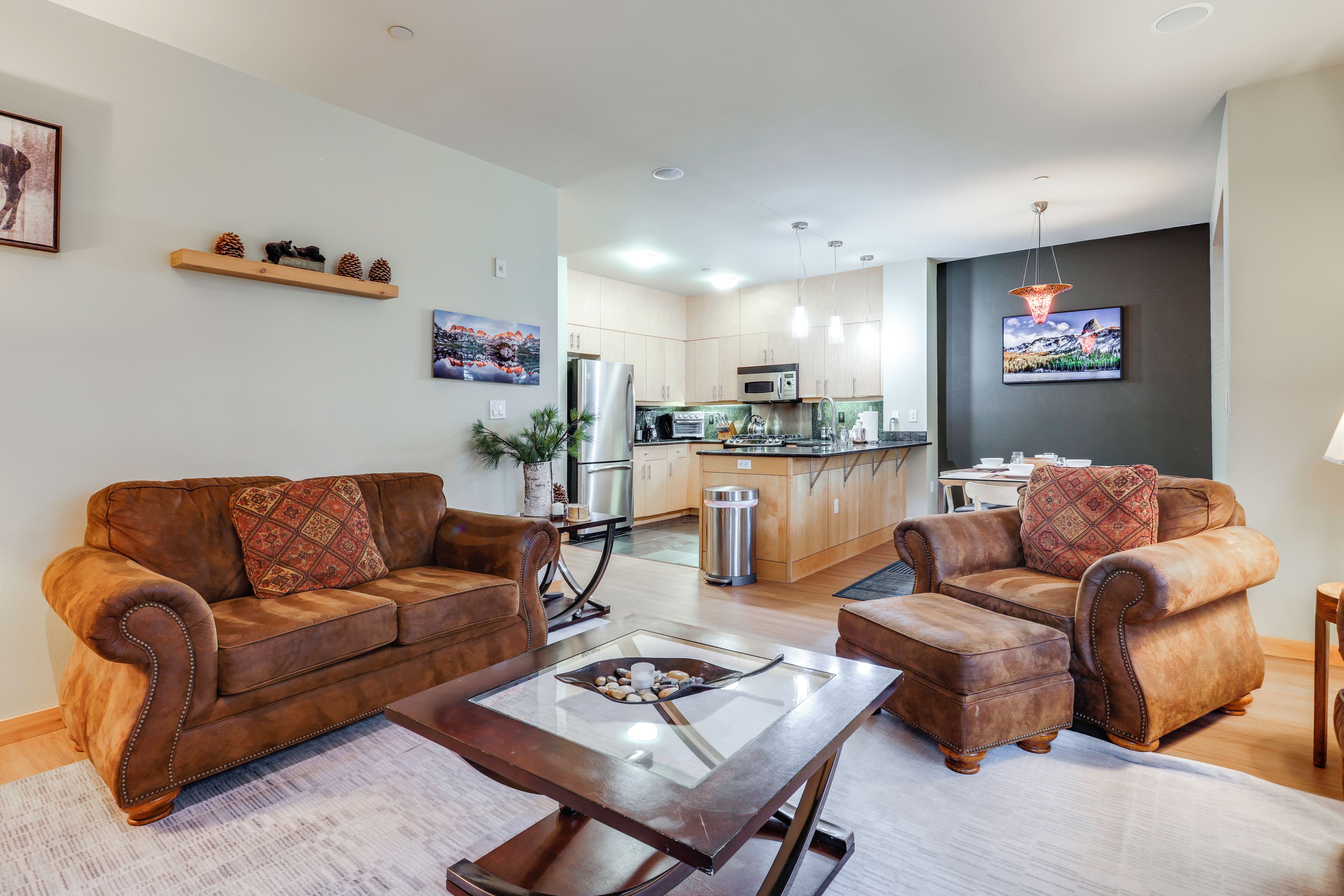 A modern living room with a brown leather sofa set, a glass coffee table, and a kitchen in the background.