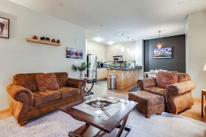 Een moderne woonkamer met een bruine leren zithoek, een glazen salontafel en een keuken op de achtergrond.