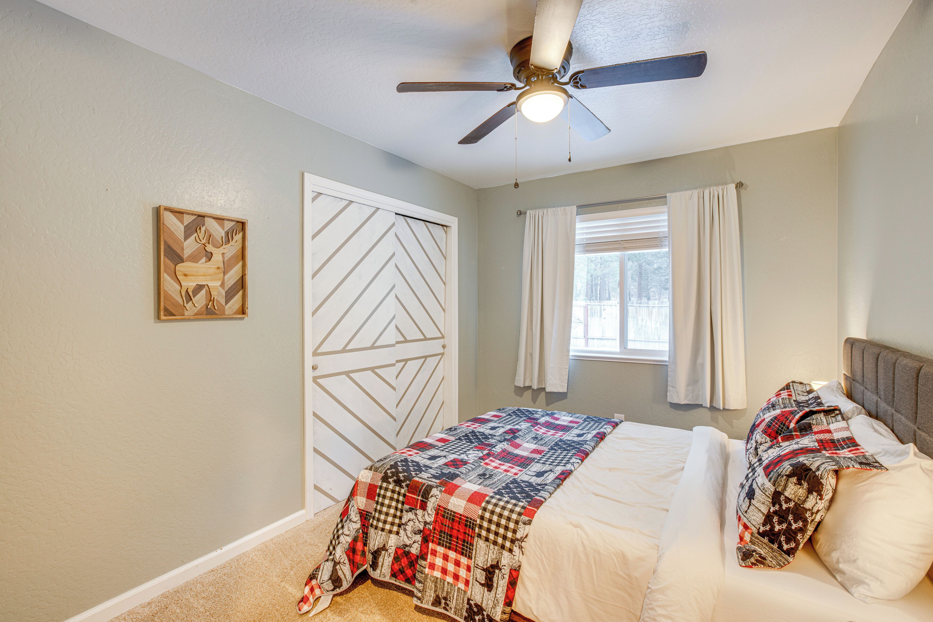 Une chambre à coucher avec un lit, un ventilateur de plafond, une fenêtre avec des rideaux et une porte ornée d’un motif géométrique.