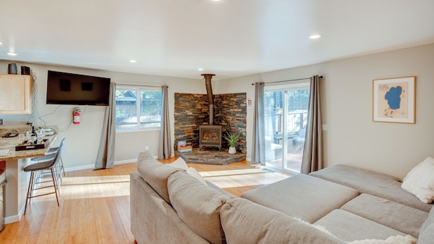 A modern living room with a stone fireplace, a sofa, a dining area with a table and chairs, and a television mounted on the wall. - Ski & Board in South Lake Tahoe! Updated Home (South Lake Tahoe)