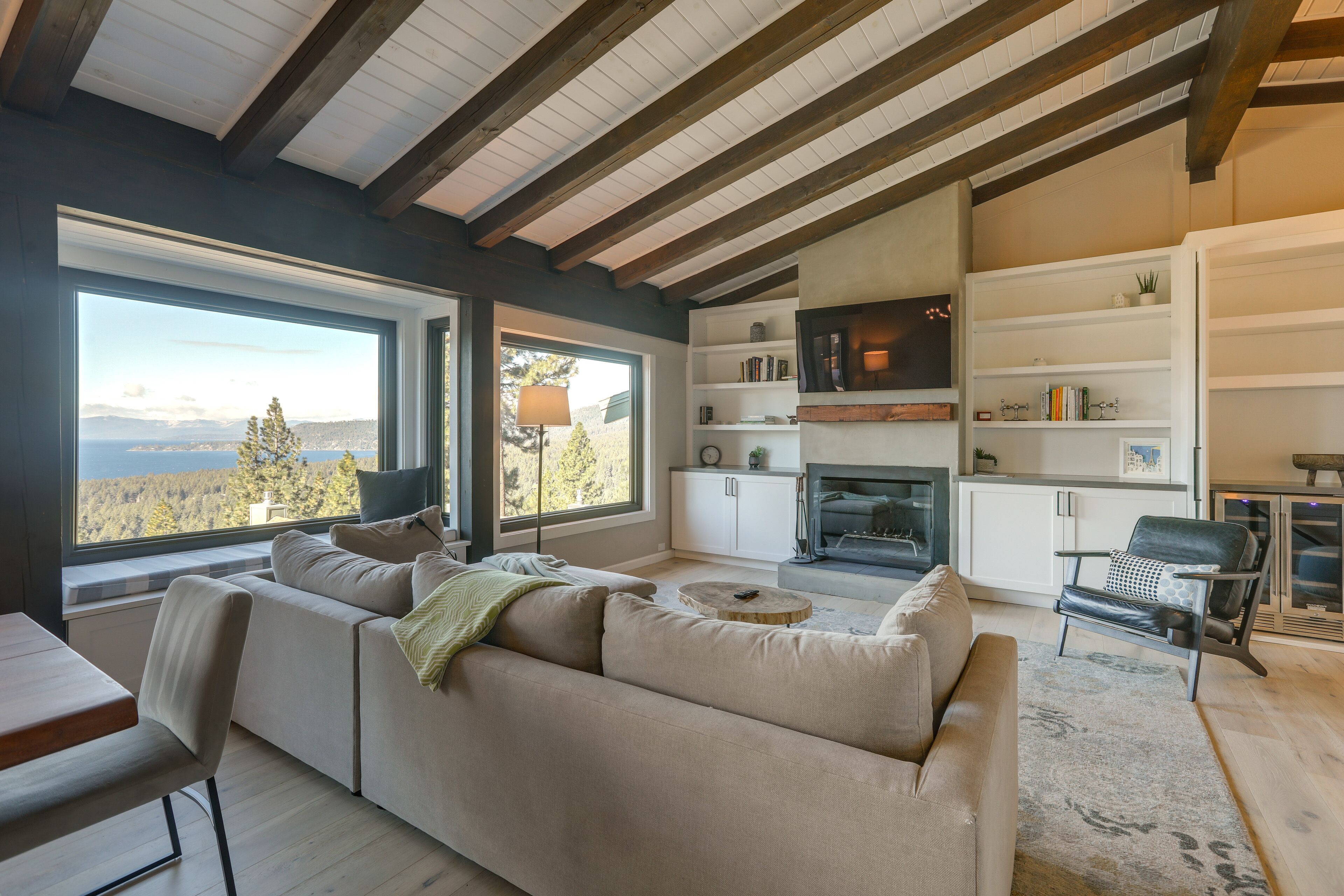 A modern living room with a large window, a sofa, a dining table, and a fireplace.