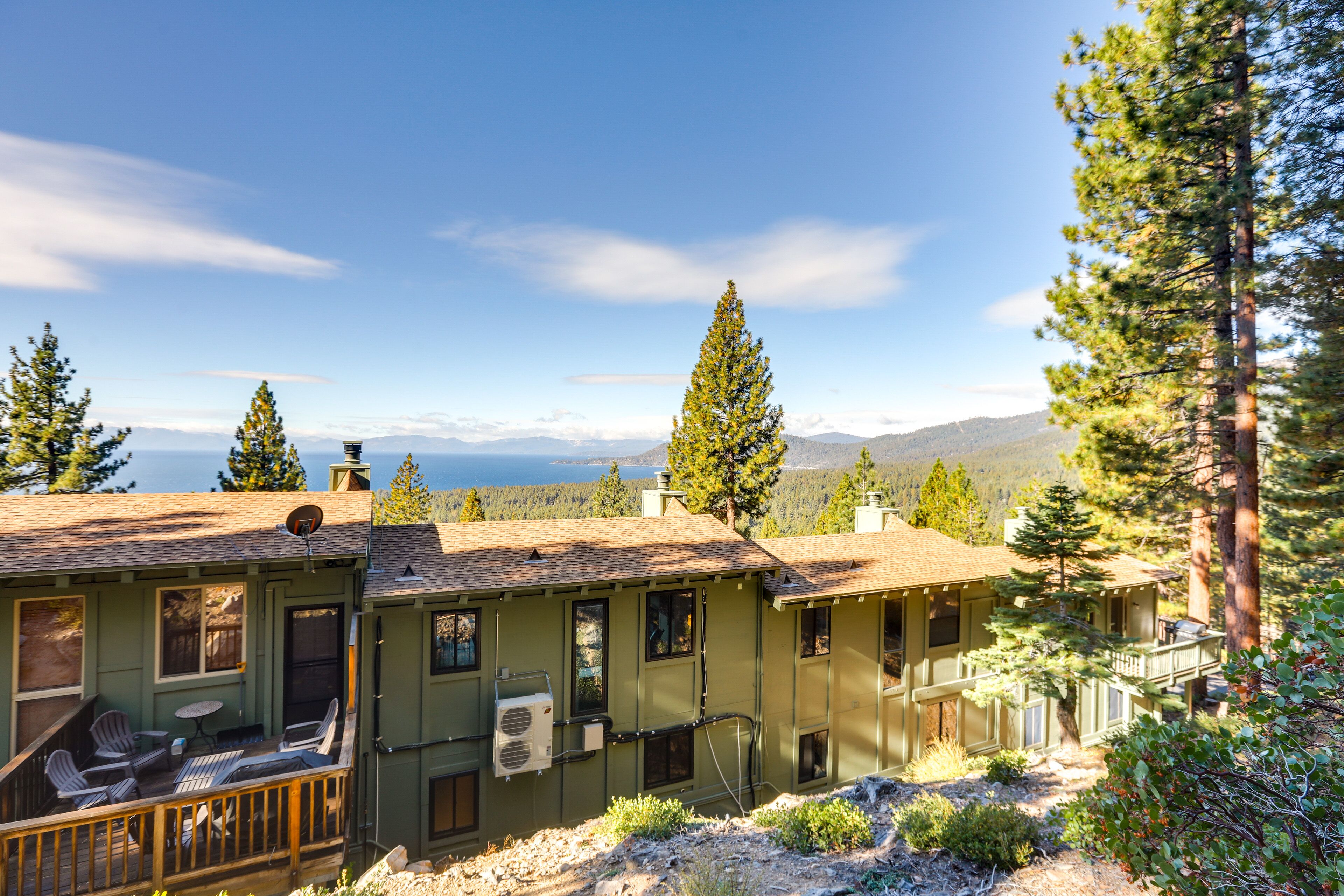 A two-story house with a deck, outdoor seating, and a view of mountains and a lake.