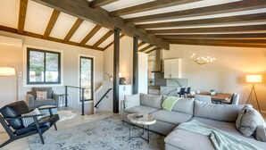 En moderne stue med en stor modulsofa, et rundt sofabord og en læderlænestol. Der er en trappe til et øvre plan, og et spiseområde med bord og stole.
