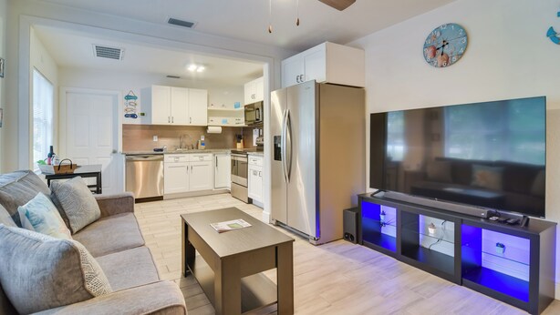 A modern living room with a sofa, coffee table, TV, and a kitchen in the background. - Walk to Art District + Beach: Pet-friendly Getaway (St. Petersburg)