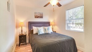 A bedroom with a bed, two bedside lamps, a ceiling fan, a window, and a painting on the wall. - Walk to Art District + Beach: Pet-friendly Getaway (St. Petersburg)